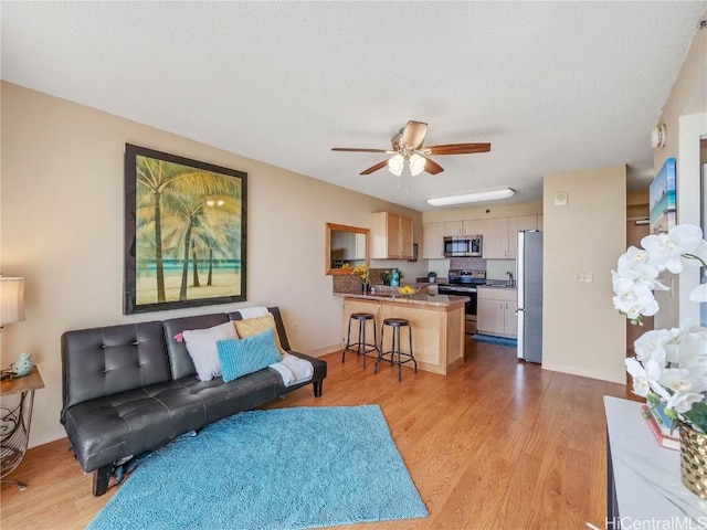 living room with light wood-type flooring, ceiling fan, and a textured ceiling