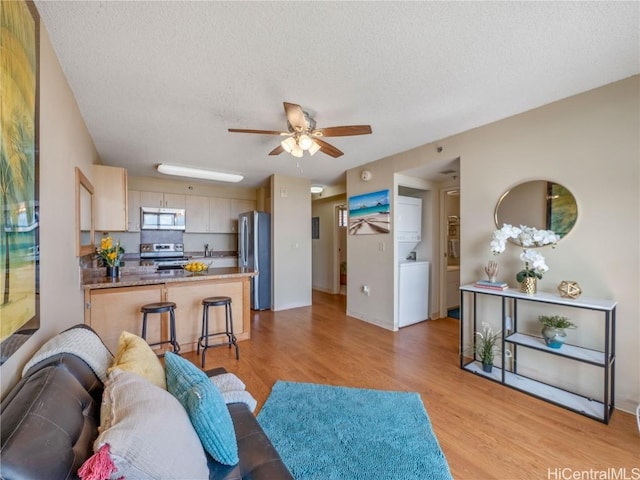 living room with a textured ceiling, ceiling fan, and light wood-type flooring