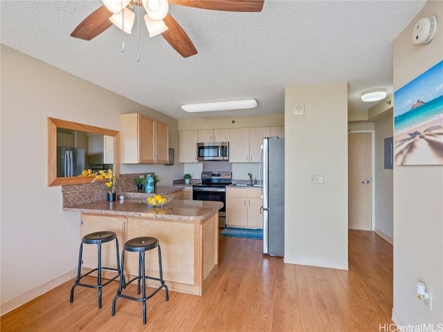 kitchen featuring ceiling fan, kitchen peninsula, appliances with stainless steel finishes, a breakfast bar area, and a textured ceiling