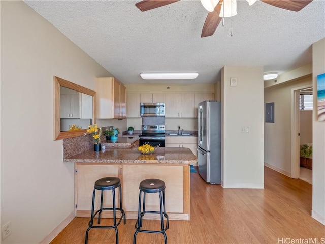 kitchen featuring appliances with stainless steel finishes, kitchen peninsula, ceiling fan, light hardwood / wood-style flooring, and a breakfast bar area