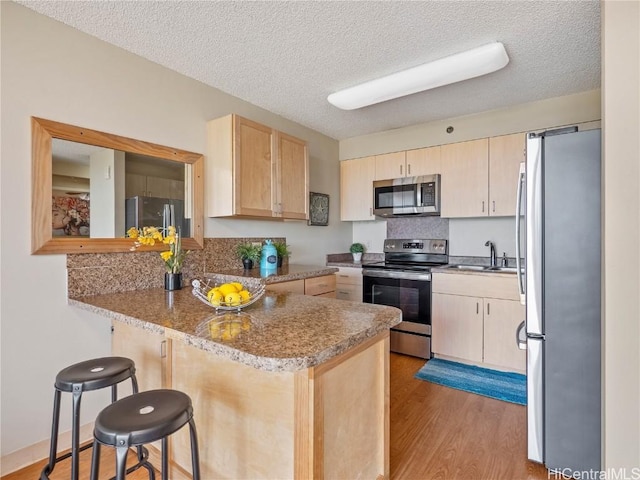 kitchen with light hardwood / wood-style floors, kitchen peninsula, sink, stainless steel appliances, and a textured ceiling