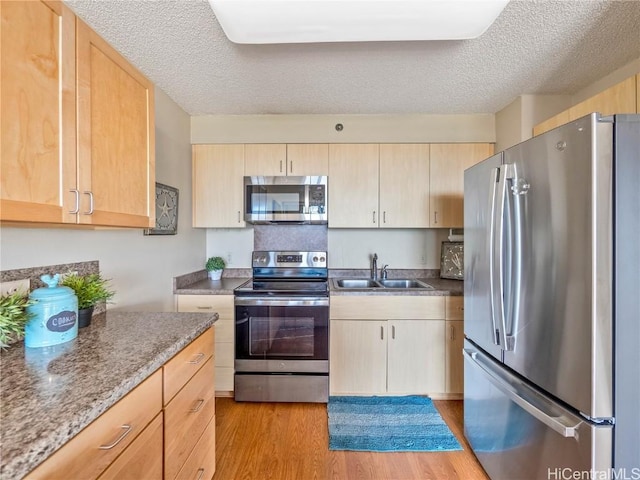 kitchen with a textured ceiling, appliances with stainless steel finishes, light brown cabinetry, and sink