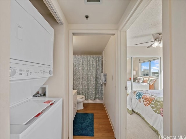 bathroom with toilet, ceiling fan, stacked washer / dryer, wood-type flooring, and vanity