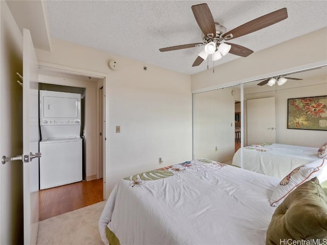 carpeted bedroom featuring ceiling fan, a textured ceiling, and stacked washing maching and dryer