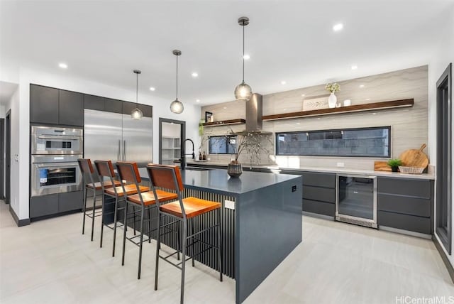 kitchen featuring wine cooler, decorative backsplash, hanging light fixtures, a kitchen island with sink, and a breakfast bar area