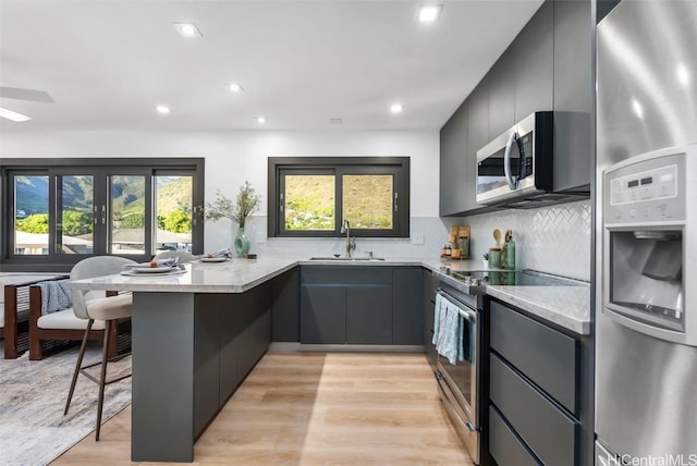 kitchen with a breakfast bar, kitchen peninsula, sink, light hardwood / wood-style flooring, and stainless steel appliances