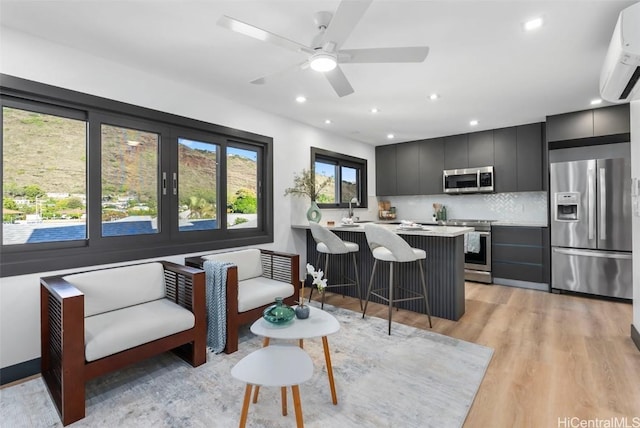 kitchen with a wall mounted AC, stainless steel appliances, backsplash, light hardwood / wood-style flooring, and a breakfast bar