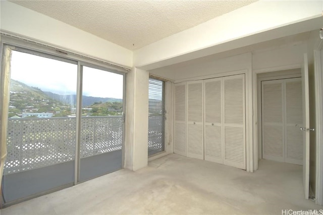 unfurnished bedroom with light carpet, a mountain view, and a textured ceiling