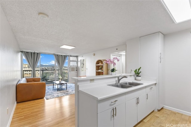 kitchen with a textured ceiling, white cabinetry, sink, kitchen peninsula, and light wood-type flooring