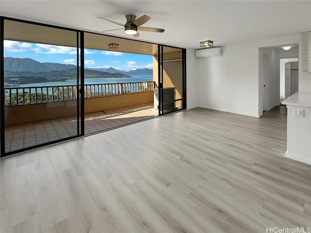 empty room featuring ceiling fan, light hardwood / wood-style floors, a water and mountain view, and an AC wall unit