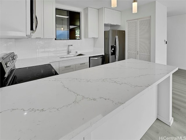 kitchen featuring appliances with stainless steel finishes, white cabinetry, sink, backsplash, and light wood-type flooring