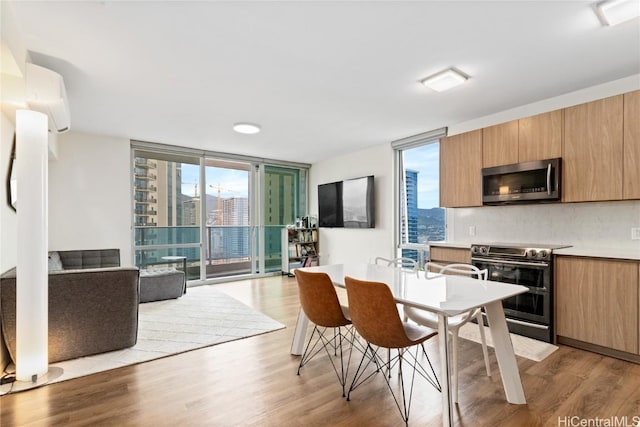 kitchen featuring appliances with stainless steel finishes, a wall of windows, decorative backsplash, a wall mounted air conditioner, and light hardwood / wood-style flooring