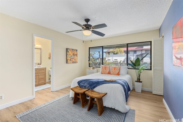 bedroom featuring ceiling fan, ensuite bath, light hardwood / wood-style flooring, and a textured ceiling