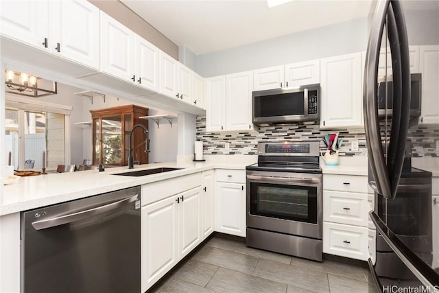 kitchen with kitchen peninsula, decorative backsplash, sink, white cabinetry, and appliances with stainless steel finishes