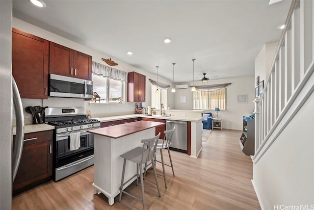 kitchen featuring a kitchen island, appliances with stainless steel finishes, pendant lighting, a breakfast bar area, and light hardwood / wood-style flooring