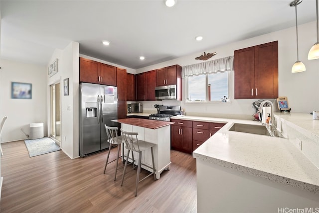 kitchen featuring sink, hanging light fixtures, light wood-type flooring, appliances with stainless steel finishes, and a kitchen island