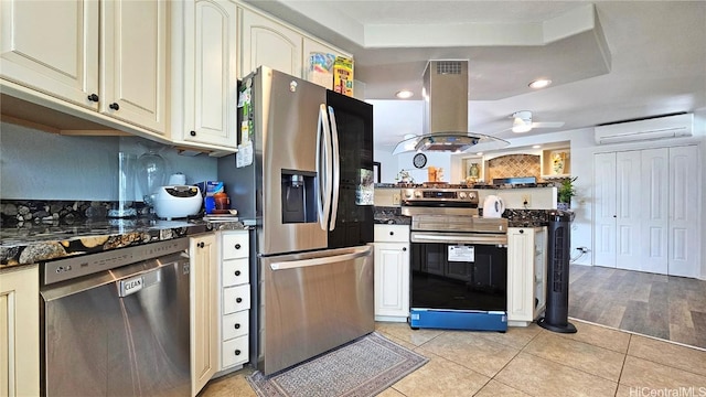 kitchen featuring appliances with stainless steel finishes, an AC wall unit, island range hood, dark stone counters, and light tile patterned floors