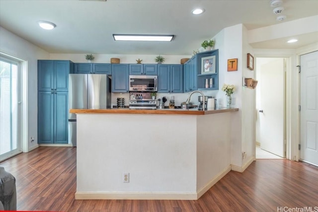 kitchen with blue cabinetry, appliances with stainless steel finishes, dark hardwood / wood-style flooring, and kitchen peninsula