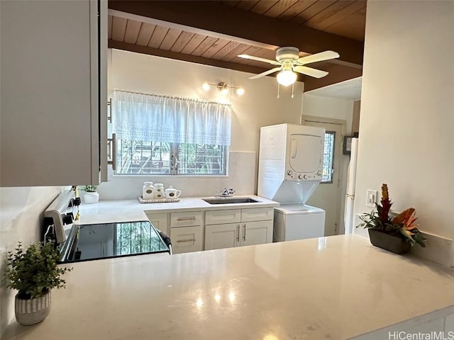 kitchen featuring stacked washer / drying machine, beamed ceiling, range, white cabinets, and sink