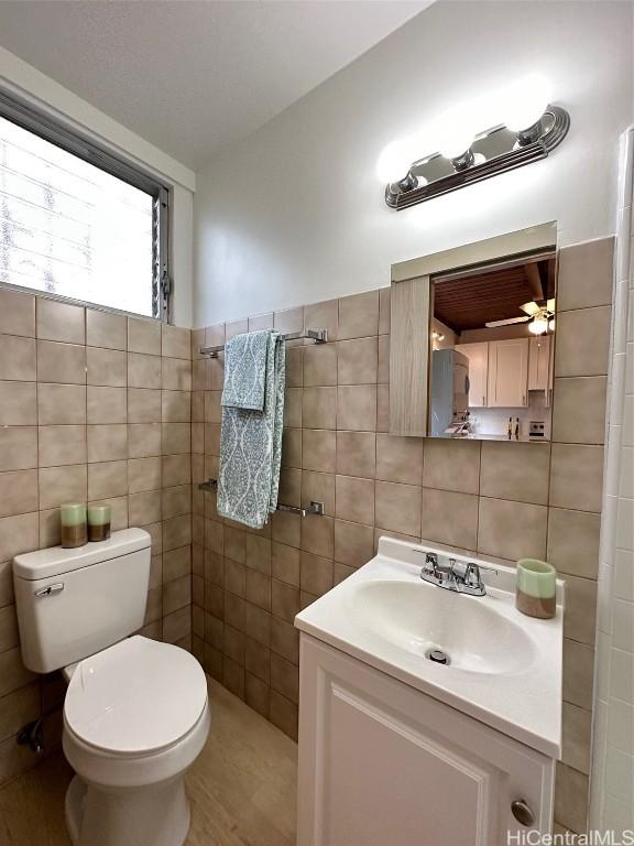 bathroom featuring toilet, tile walls, and vanity