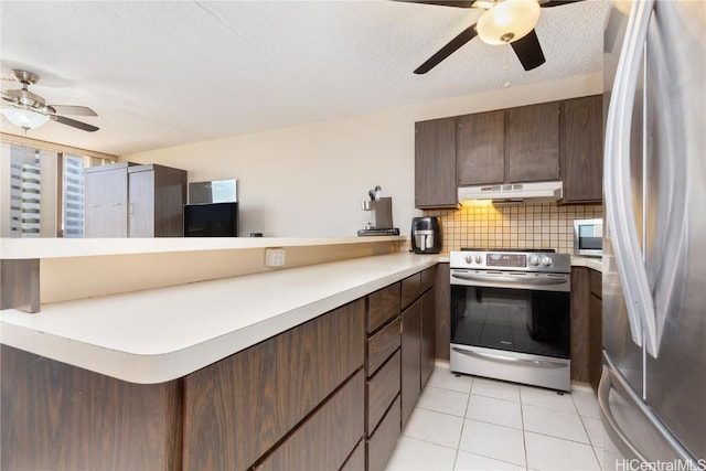 kitchen featuring kitchen peninsula, decorative backsplash, dark brown cabinetry, stainless steel appliances, and light tile patterned floors