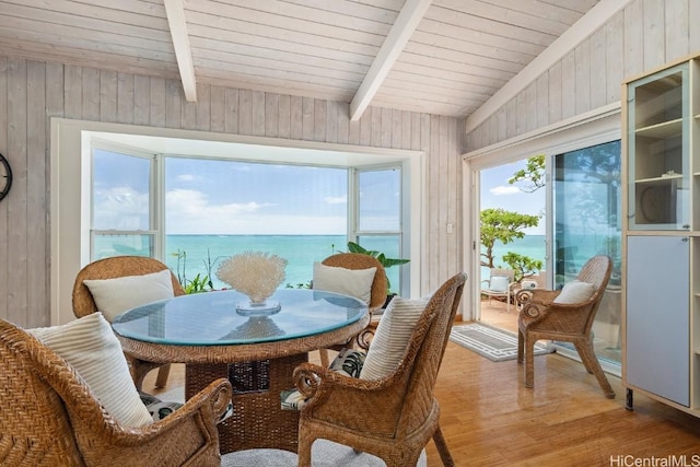 dining space with wood walls, wooden ceiling, a water view, light hardwood / wood-style flooring, and beamed ceiling