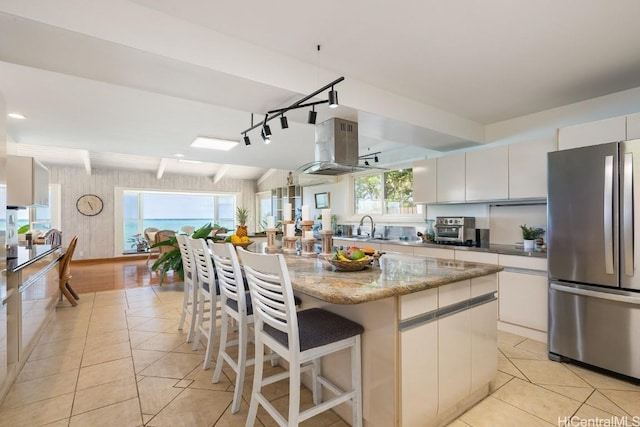 kitchen with light tile patterned floors, white cabinetry, stainless steel refrigerator, beam ceiling, and a center island