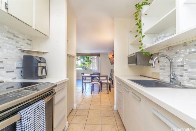 kitchen featuring white cabinets, stainless steel range with electric cooktop, decorative backsplash, sink, and light tile patterned floors