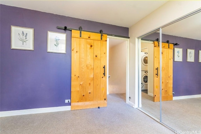 unfurnished bedroom with carpet flooring, a closet, stacked washer and dryer, and a barn door