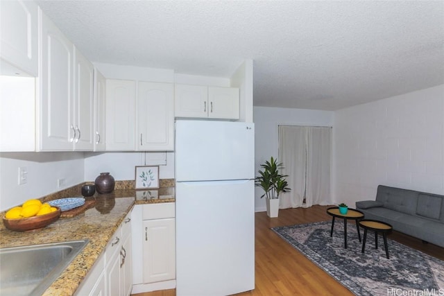 kitchen featuring white cabinets, light wood-type flooring, white fridge, and a textured ceiling