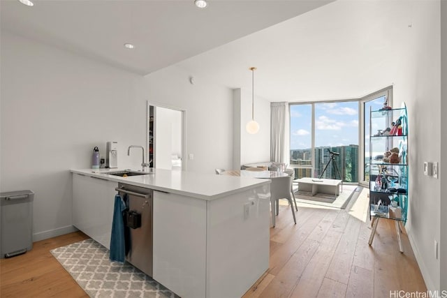 kitchen with a peninsula, a sink, light wood-style floors, dishwasher, and a wall of windows