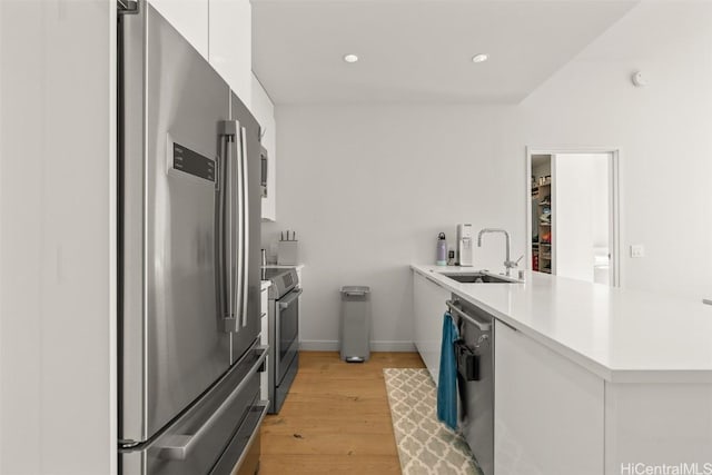 kitchen featuring light countertops, appliances with stainless steel finishes, white cabinets, a sink, and a peninsula