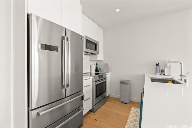 kitchen with a sink, white cabinetry, light wood-style floors, light countertops, and appliances with stainless steel finishes