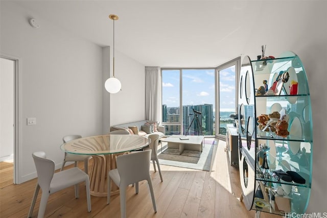 dining area featuring light wood-style floors, a view of city, baseboards, and a wall of windows