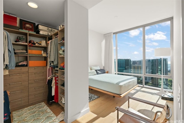 bedroom with a view of city, a closet, wood finished floors, and floor to ceiling windows