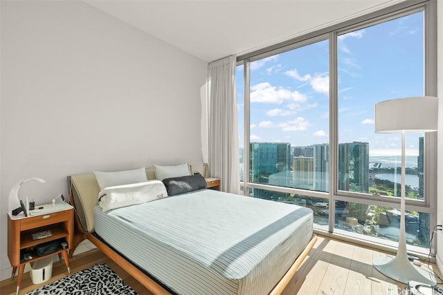 bedroom with floor to ceiling windows, a city view, and wood finished floors