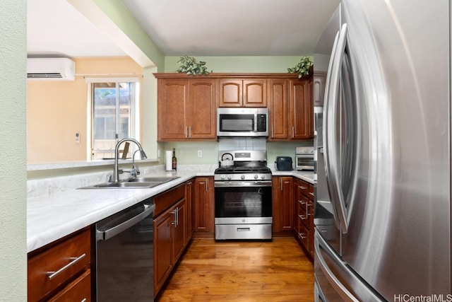 kitchen featuring light hardwood / wood-style floors, a wall unit AC, appliances with stainless steel finishes, tasteful backsplash, and sink