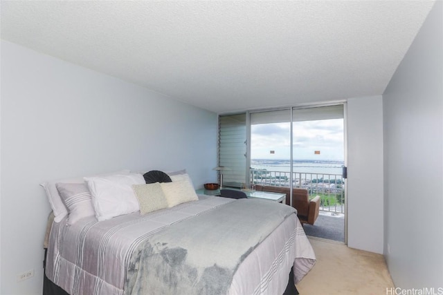 bedroom featuring a textured ceiling, light colored carpet, access to exterior, and a wall of windows