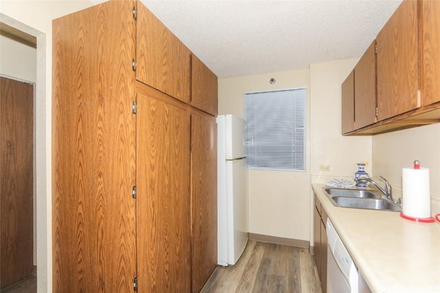 kitchen with sink, a textured ceiling, white appliances, and light hardwood / wood-style floors