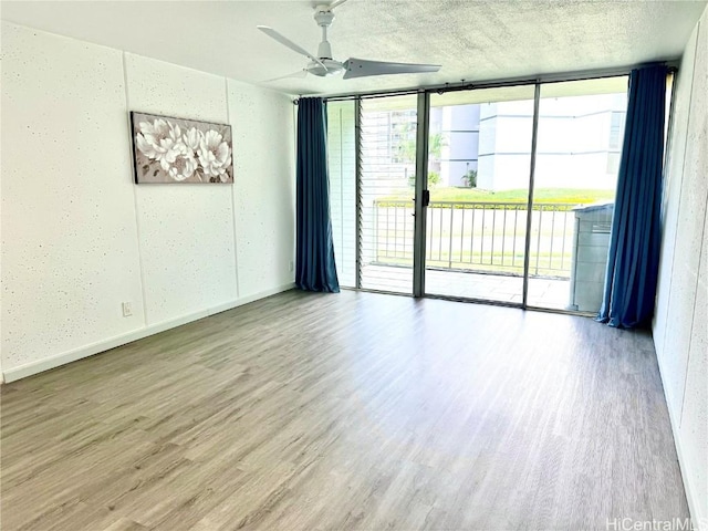 empty room with a textured ceiling, floor to ceiling windows, ceiling fan, and light wood-type flooring