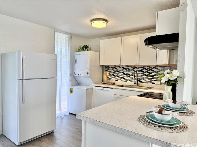 kitchen with white cabinetry, sink, decorative backsplash, stacked washer and dryer, and white appliances