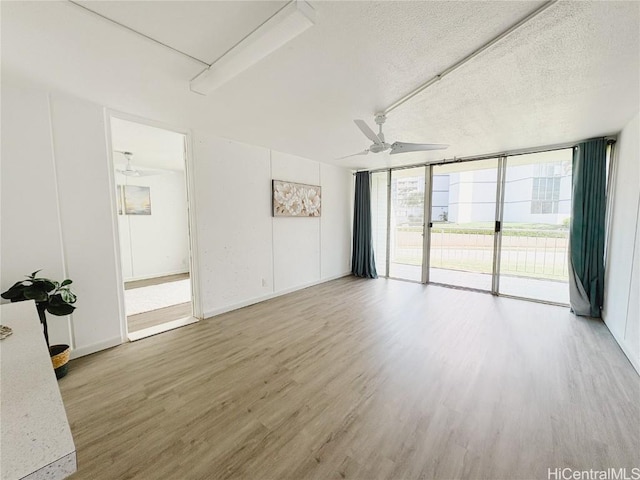 empty room featuring ceiling fan, floor to ceiling windows, hardwood / wood-style floors, and a textured ceiling