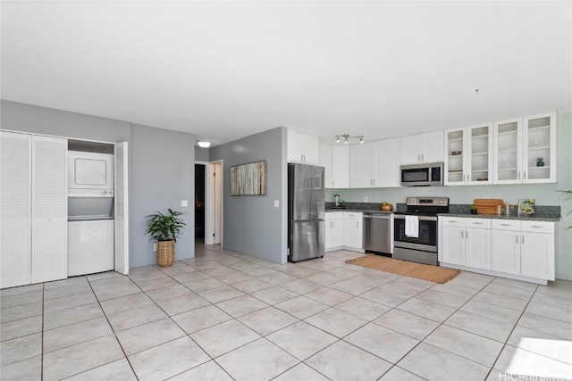 kitchen with white cabinetry, stacked washer and clothes dryer, stainless steel appliances, and light tile patterned flooring