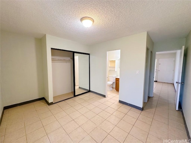 unfurnished bedroom with ensuite bath, light tile patterned floors, a closet, and a textured ceiling