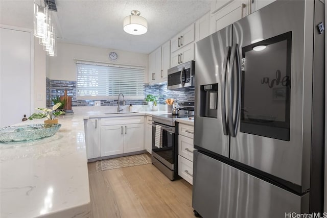 kitchen with a textured ceiling, appliances with stainless steel finishes, decorative light fixtures, white cabinetry, and sink