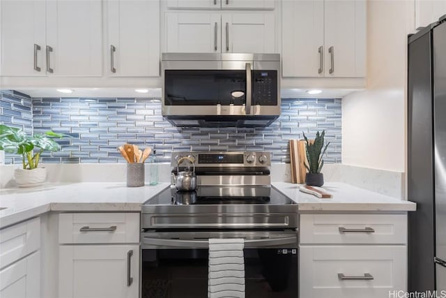 kitchen with appliances with stainless steel finishes, backsplash, white cabinetry, and light stone countertops