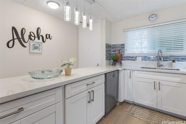 kitchen with decorative light fixtures, stainless steel dishwasher, sink, light wood-type flooring, and white cabinets