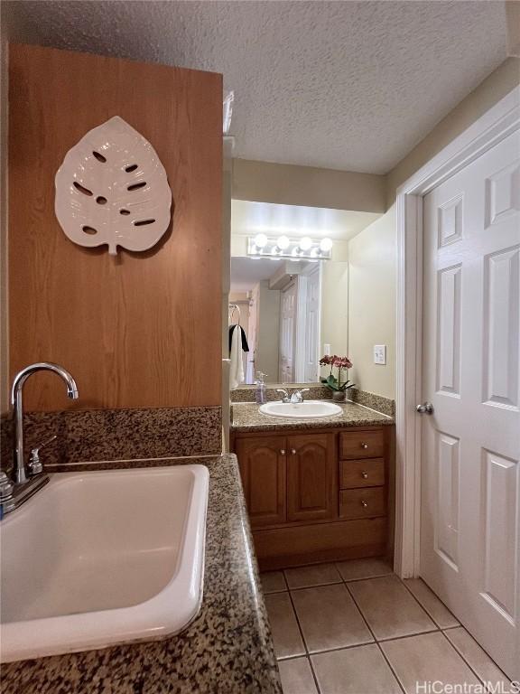 bathroom featuring a textured ceiling, tile patterned flooring, a tub to relax in, and vanity