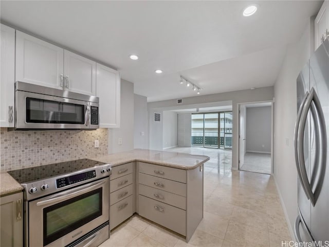 kitchen with kitchen peninsula, backsplash, white cabinets, light stone counters, and stainless steel appliances