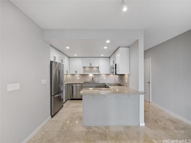 kitchen featuring light stone countertops, appliances with stainless steel finishes, white cabinetry, sink, and kitchen peninsula